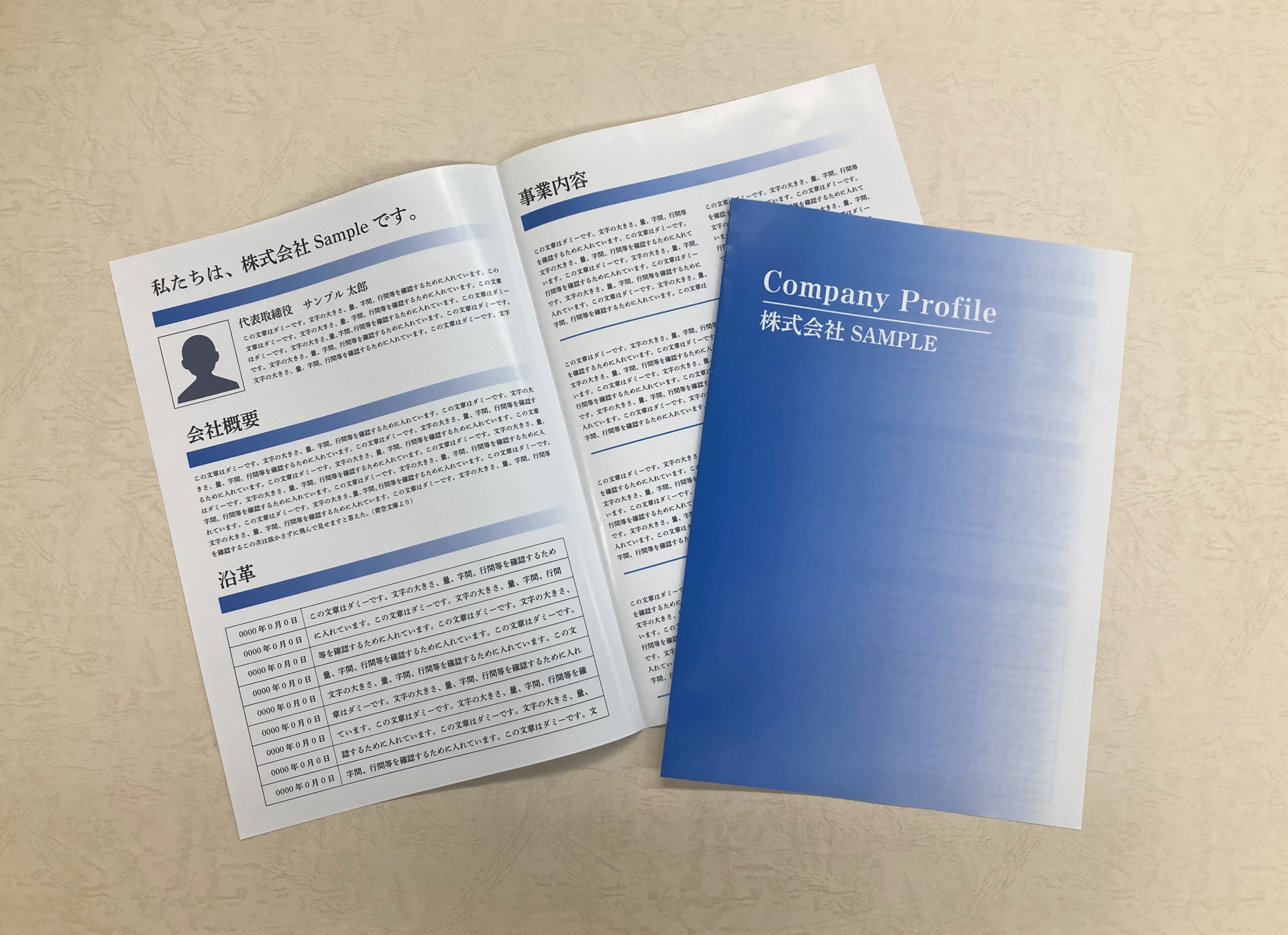 Open corporate documents with a blue gradient cover reading 'Company Profile' on top of white pages with Japanese text, laid on a beige textured surface.