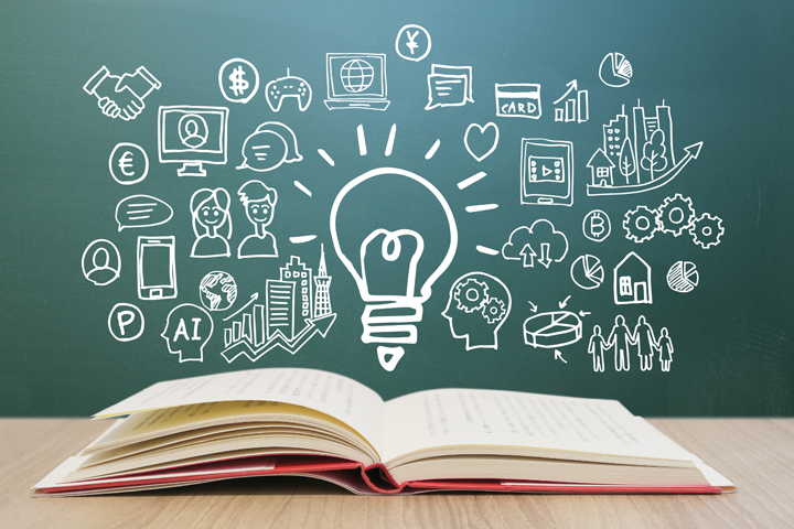 Open book on a table with a chalkboard full of lightbulb and business icons, representing ideas and learning.