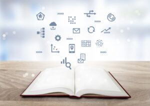 Open book on a wooden table with blue digital icons floating above, symbolizing learning and ideas.