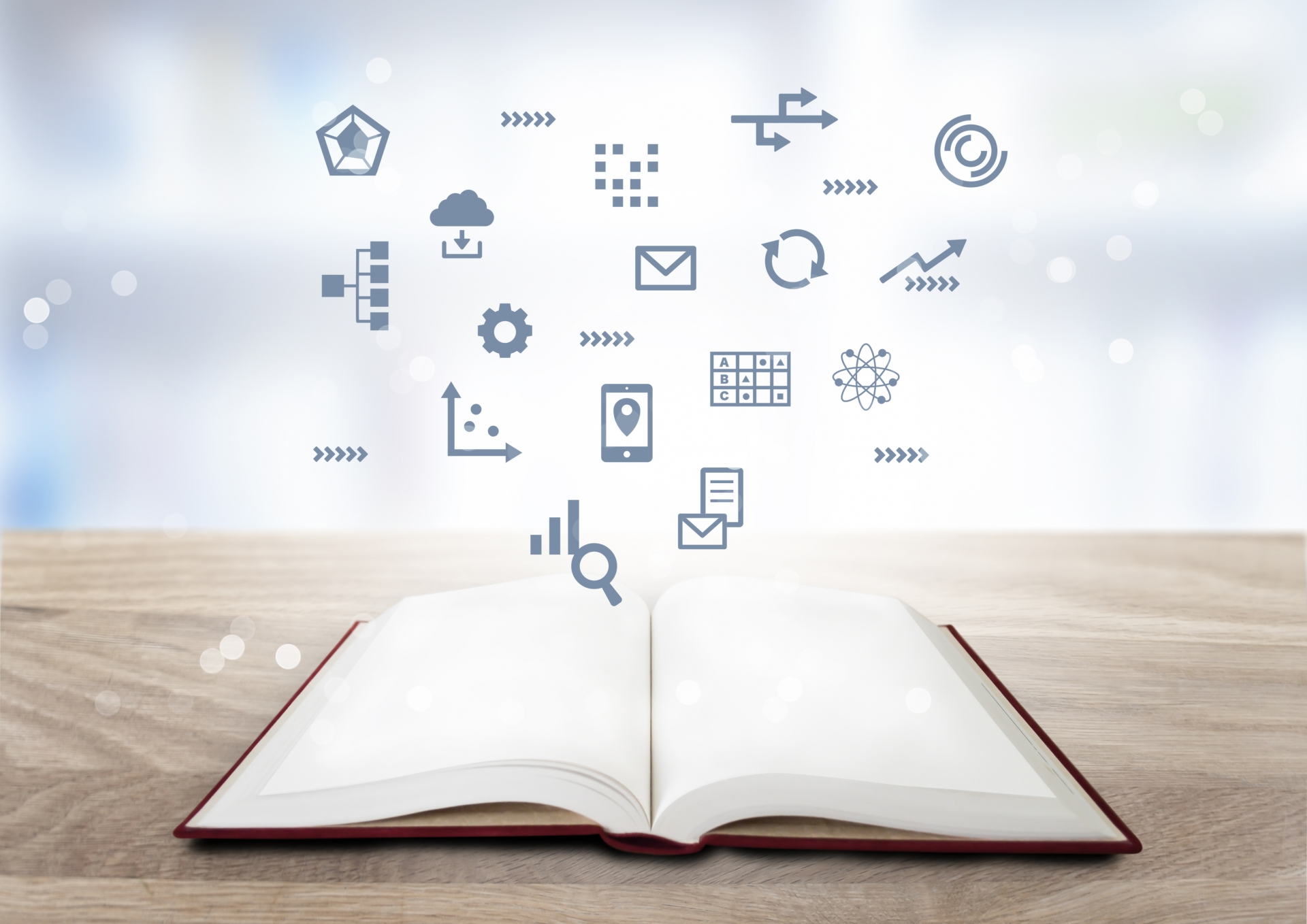 Open book on a wooden table with blue digital icons floating above, symbolizing learning and ideas.
