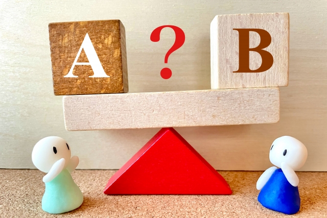Two small figurines watch a balance with A on the left, B on the right, and a red question mark between.