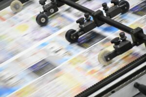 High-speed newspaper printing press with multiple rollers feeding blurred newspapers forward