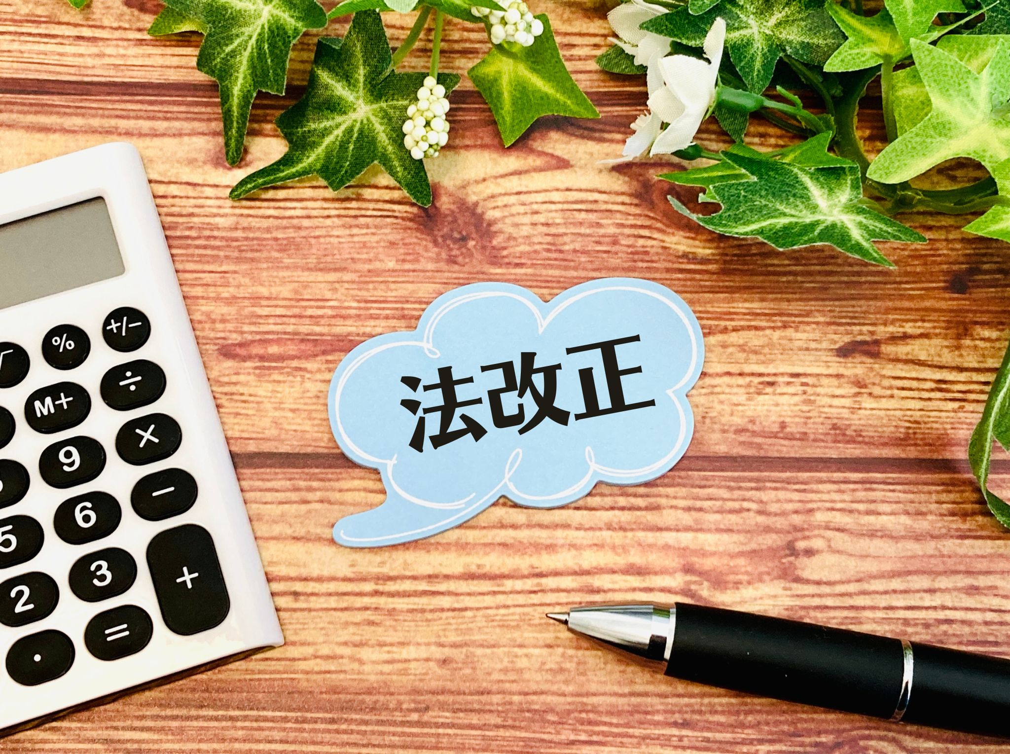 Top-down view of a wooden desk with a white calculator on the left, a black-and-silver pen at the bottom right, and a blue cloud-shaped card with black Chinese characters in the center.
