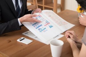 Two professionals review a printed report with colorful charts and graphs on a wooden table, with a calculator and a mug nearby.