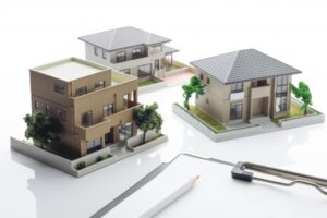 Miniature residential buildings with landscaping, a pencil, and drafting tool on a white surface, suggesting architectural planning.