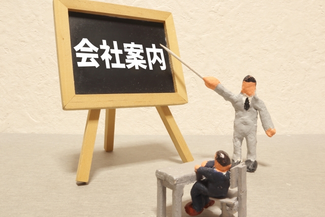 Two miniature figures present company information to a chalkboard that reads 会社案内 (company info).